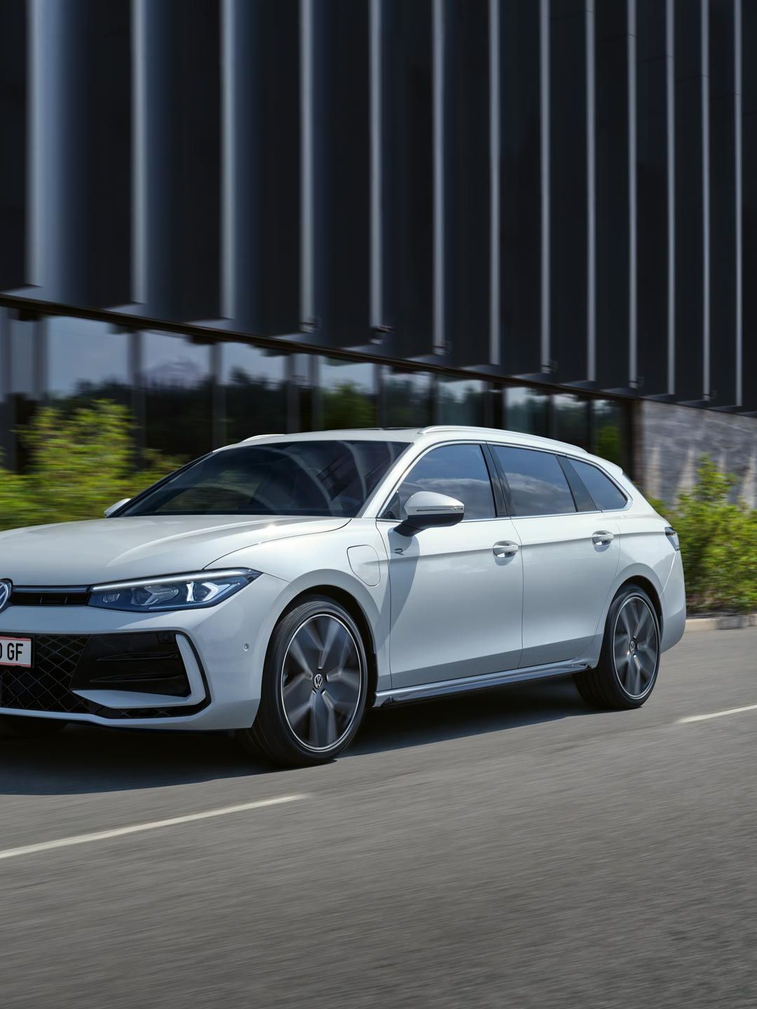 Bel VW Passat je parkiran bočno pred stavbo.