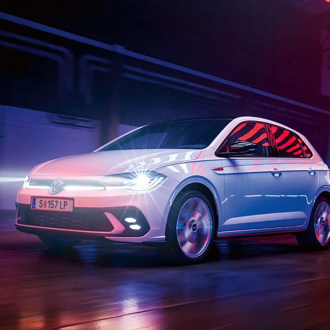 Bel VW Polo GTI z vključenimi matričnimi LED-žarometi in linijsko osvetlitvijo na sprednjem delu vozi v hali.