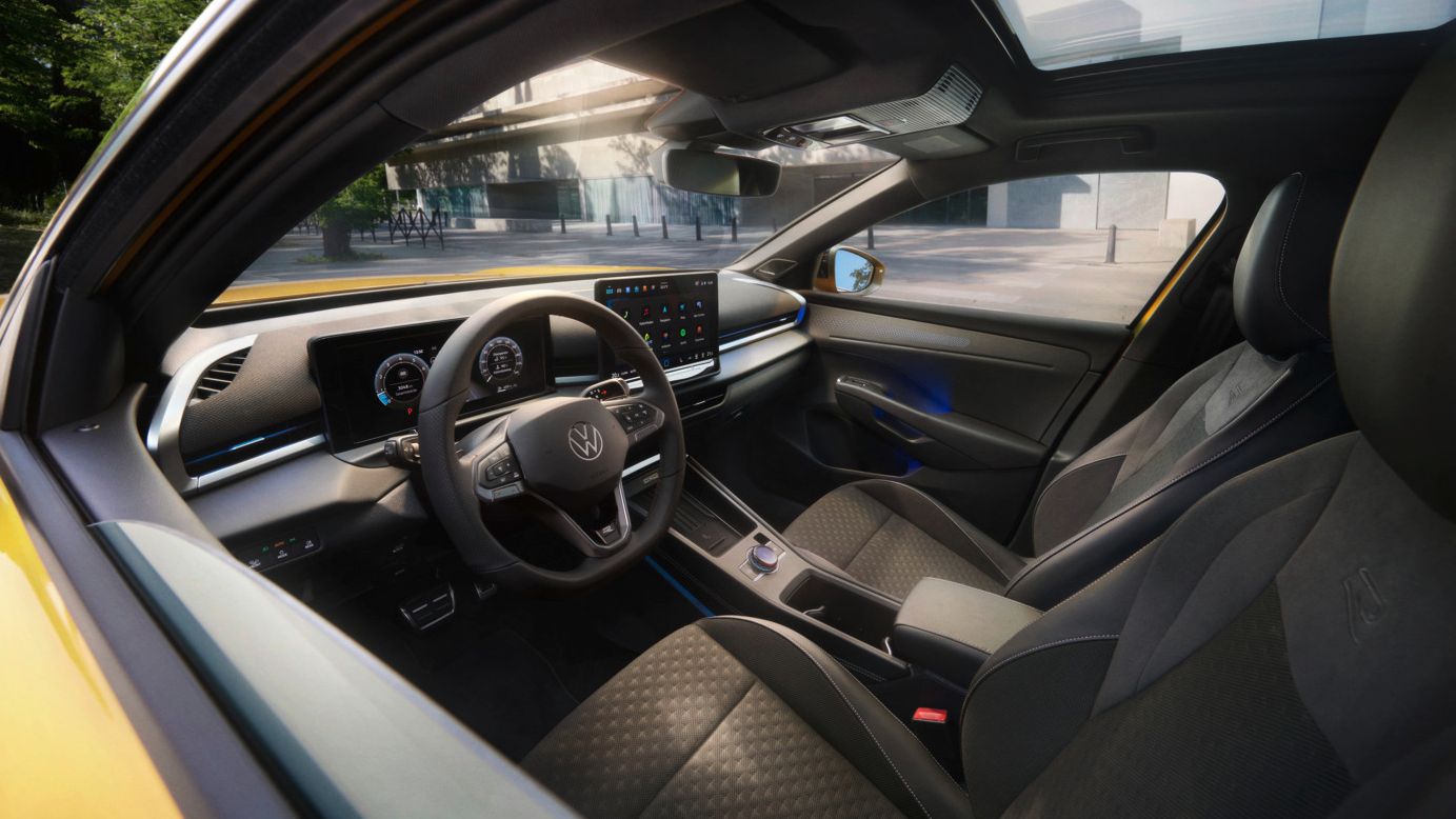 Slika prikazuje pogled v notranjost rumenega VW T-Roc. Vidite lahko dva sprednja sedeža, volan, infotainment sistem, pa tudi majhen del rumeno pobarvane zunanjosti.