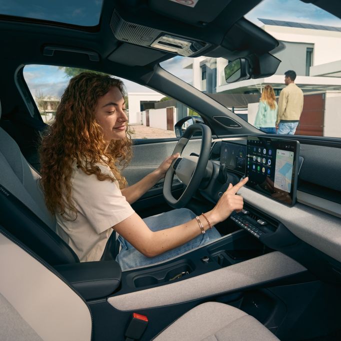 Mlada ženska sedi na voznikovem sedežu VW ID. Cross in upravlja informacijsko-zabavni sistem.