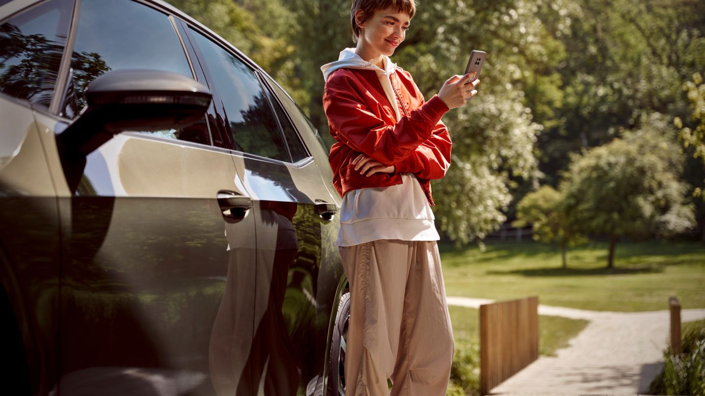 Eine Frau mit einem Smartphone steht neben ihrem ID.3