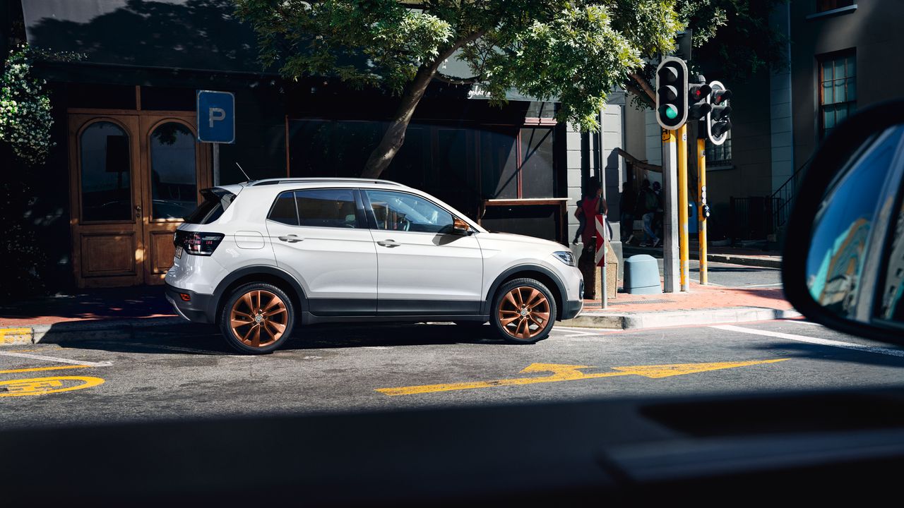 Bel VW T-Cross z opcijskim stilskim paketom Penny Copper je parkiran na ulici. Prikazana je stranska silhueta vozila, platišča in ohišji zunanjih ogledal so bakrene barve.