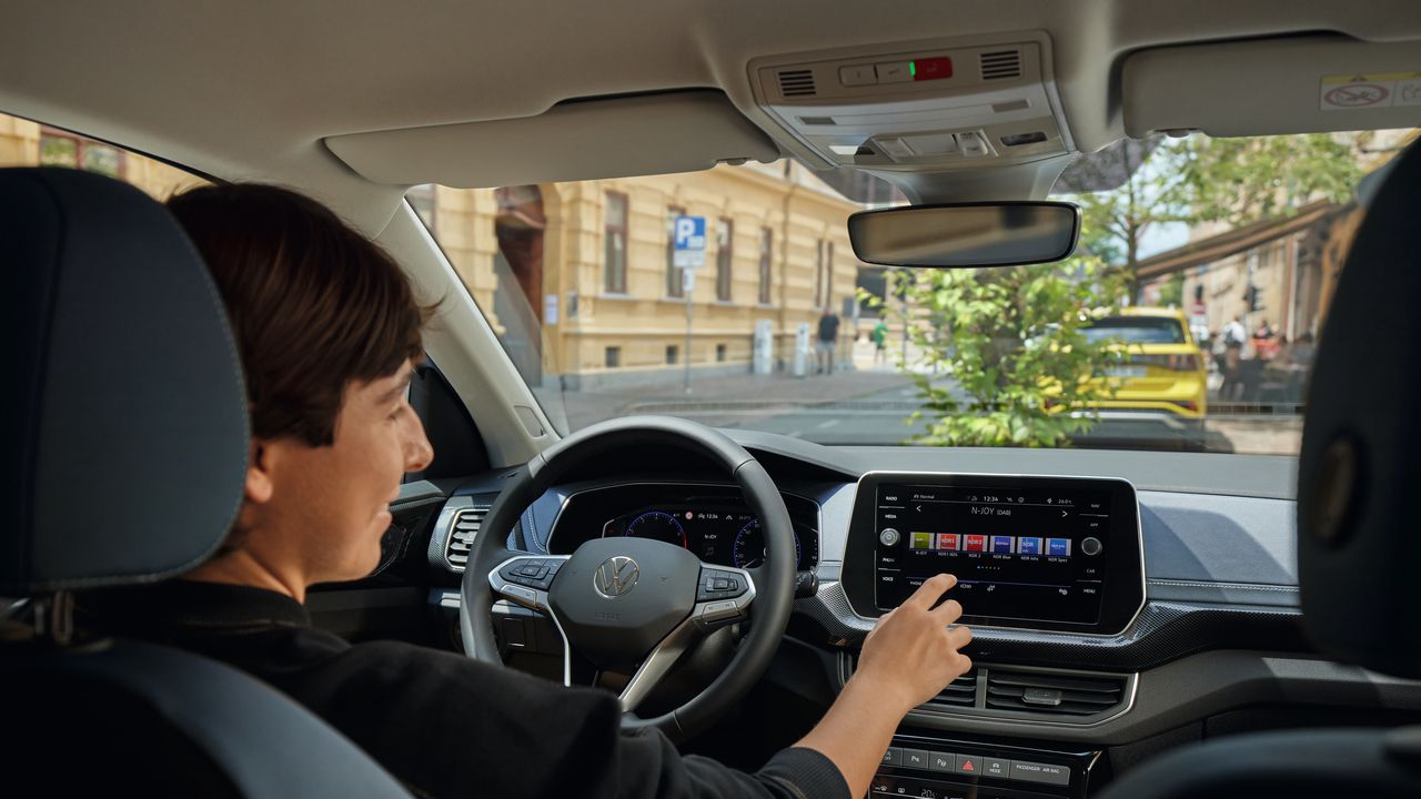 Mlajša ženska sedi na voznikovem sedežu in prek velikega zaslona infotainment sistema upravlja radio.