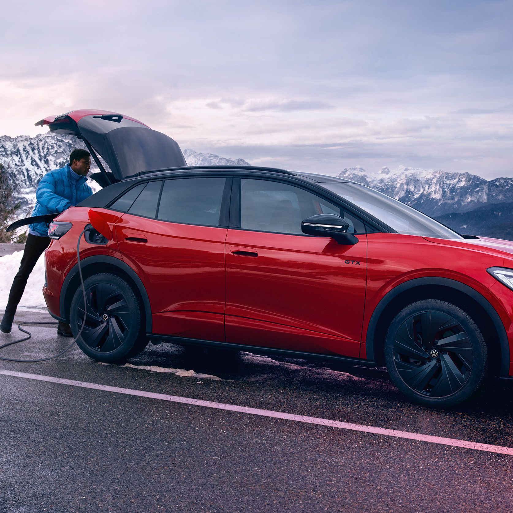 Mann öffnet Kofferraum eines VW ID.4 GTX auf einer Bergstraße