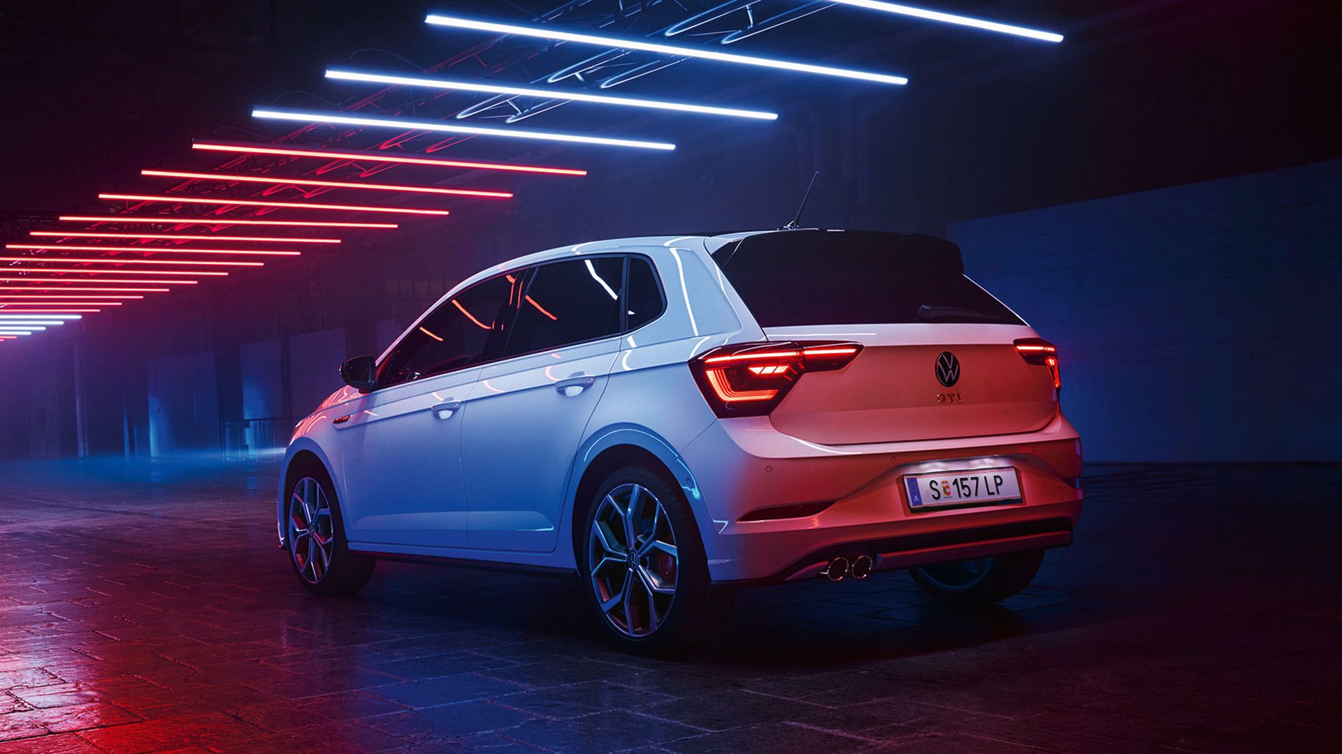Seitliche Heckansicht des VW Polo GTI, der geparkt in einer Halle steht und mit weißen und roten Lichtern angestrahlt wird