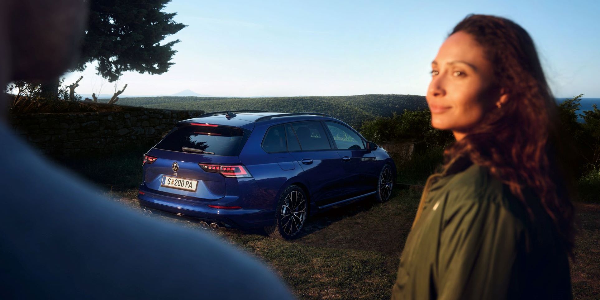 Ein roter VW Golf GTI steht vor einem Gebäude. Zwei Personen sitzen neben dem Wagen.