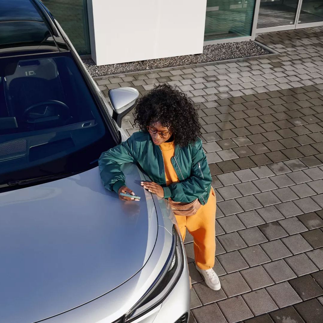 Ein VW ID. mit Blick von oben, eine Frau lehnt an der Kühlerhaube