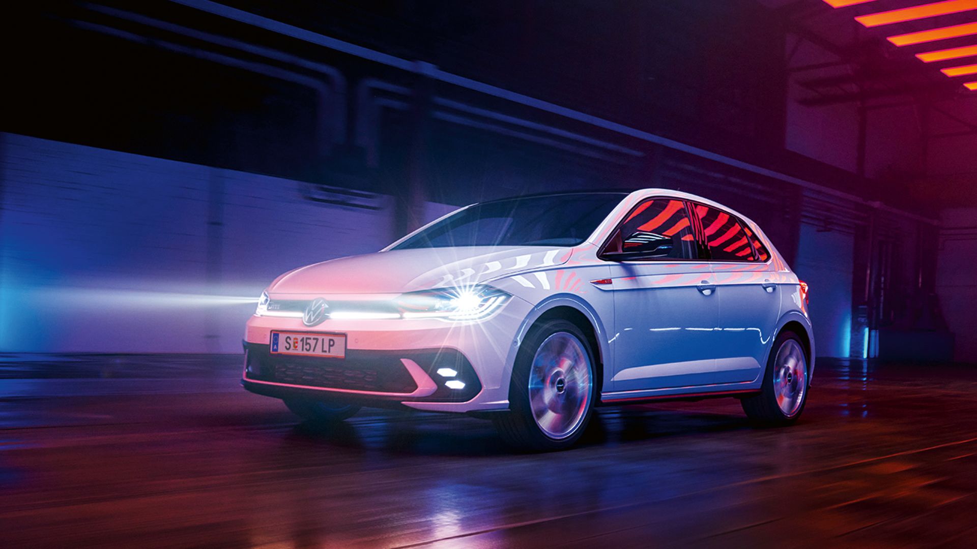 Bel VW Polo GTI z vključenimi matričnimi LED-žarometi in linijsko osvetlitvijo na sprednjem delu vozi v hali.