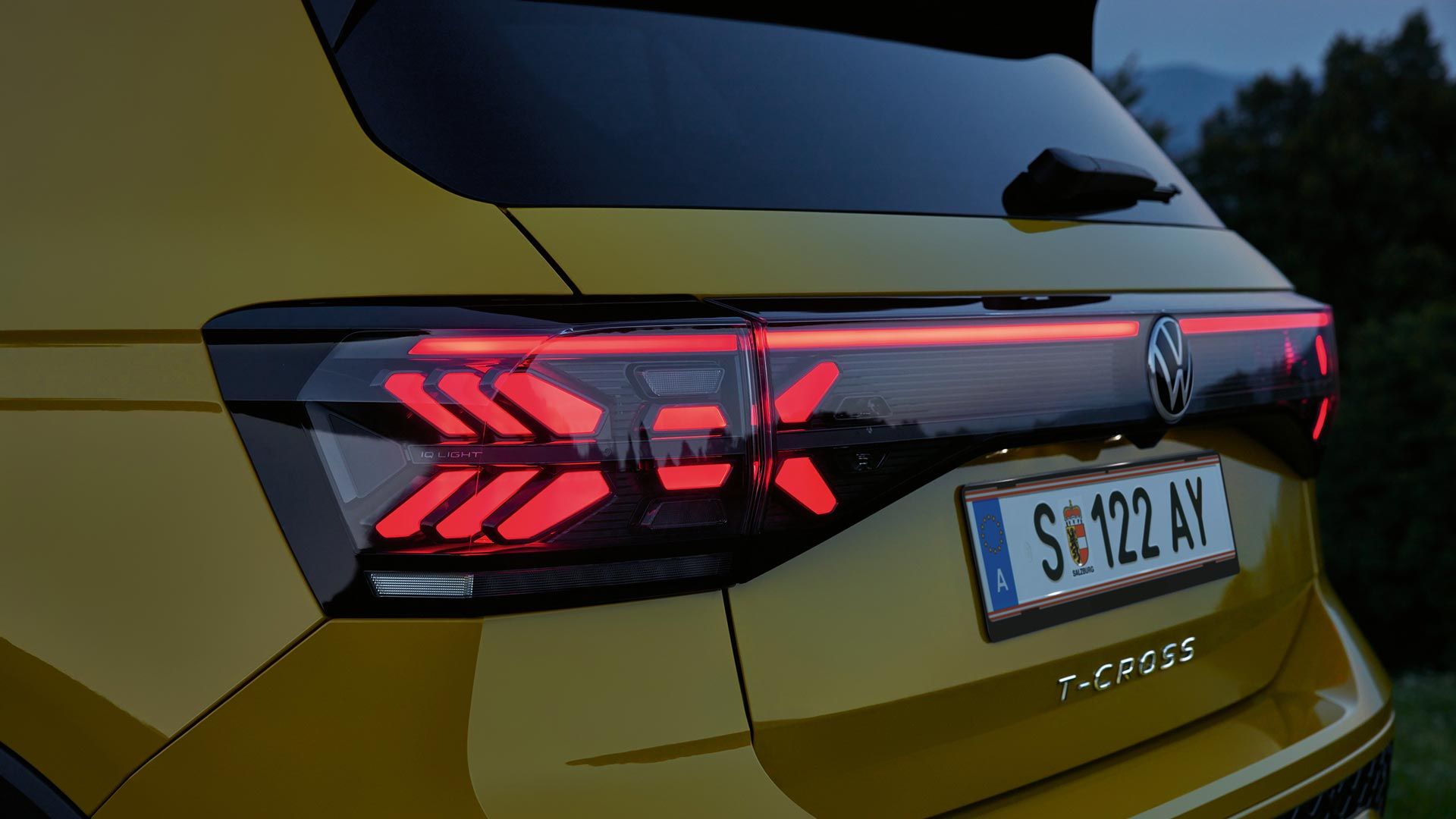 Detajlni posnetek zadnjih luči rumenega VW T-Crossa v mraku.
