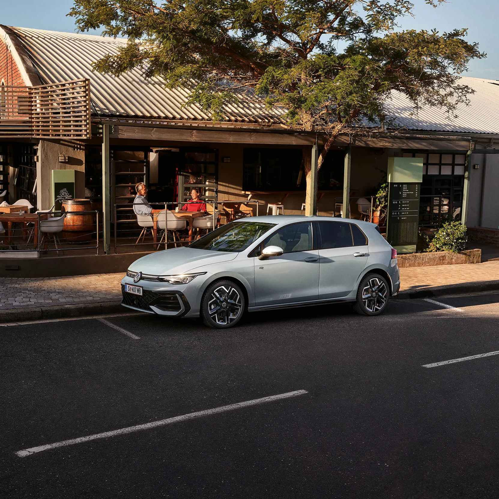 Pogled od spredaj na bel VW Golf eHybrid s priključenim polnilnim kablom, dva moška se približujeta vozilu