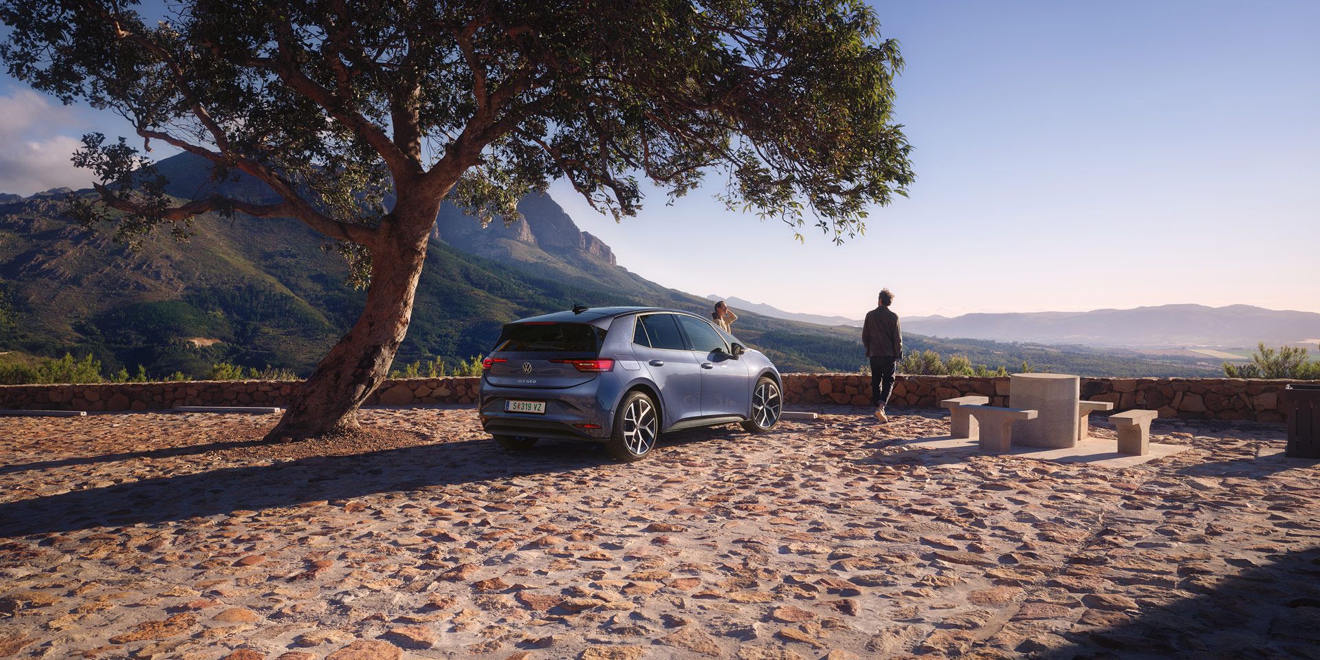 Modri VW ID.3 Neo je parkiran na parkirišču v gorah, ženska in moški uživata v razgledu