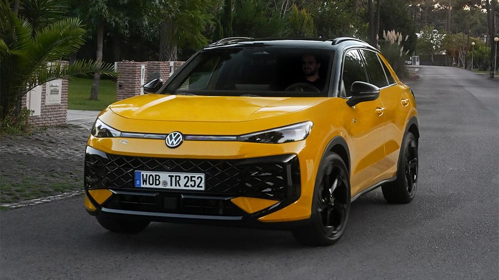 Rumen Volkswagen T-Roc vozi po asfaltirani cesti, obdani z zelenjem in drevesi. 