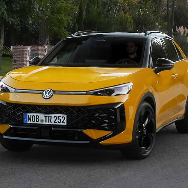Rumen Volkswagen T-Roc vozi po asfaltirani cesti, obdani z zelenjem in drevesi. 