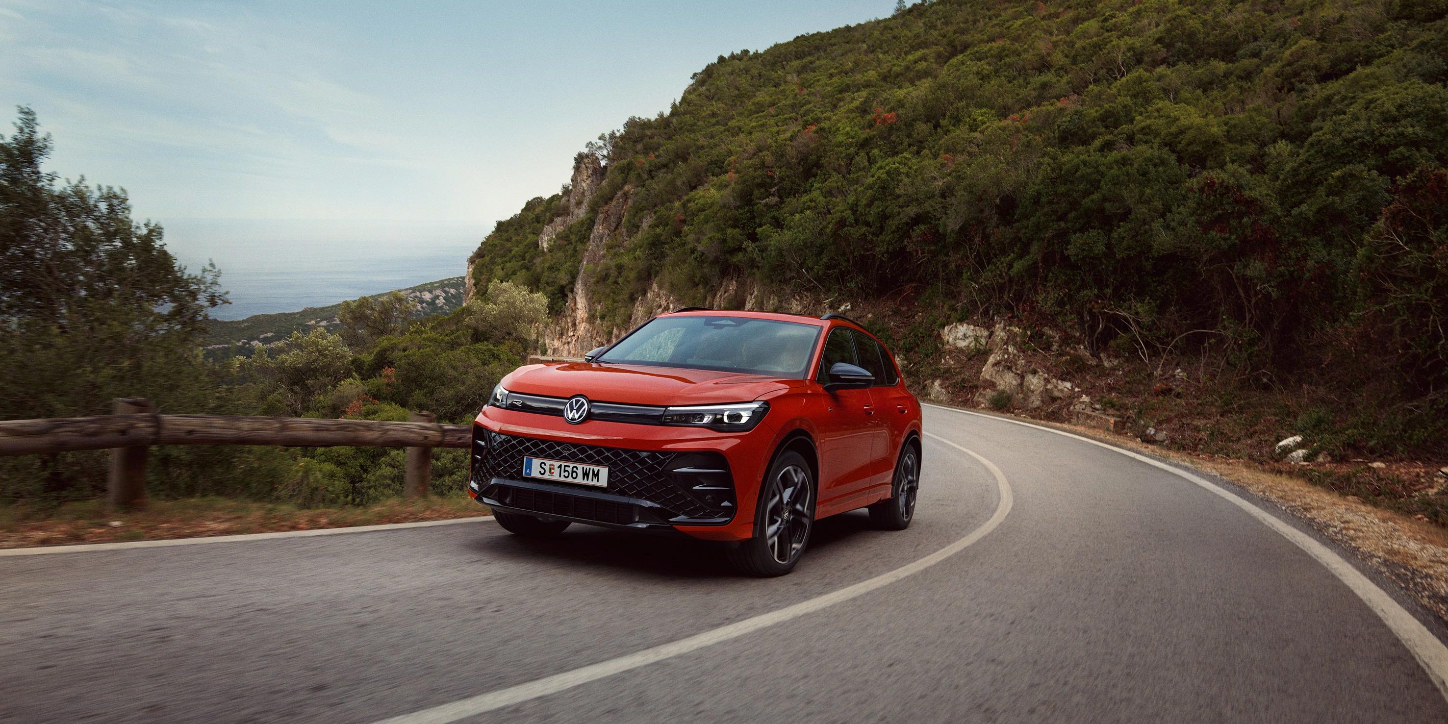 Rdeči VW Tiguan, ki vozi po ovinkasti cesti.