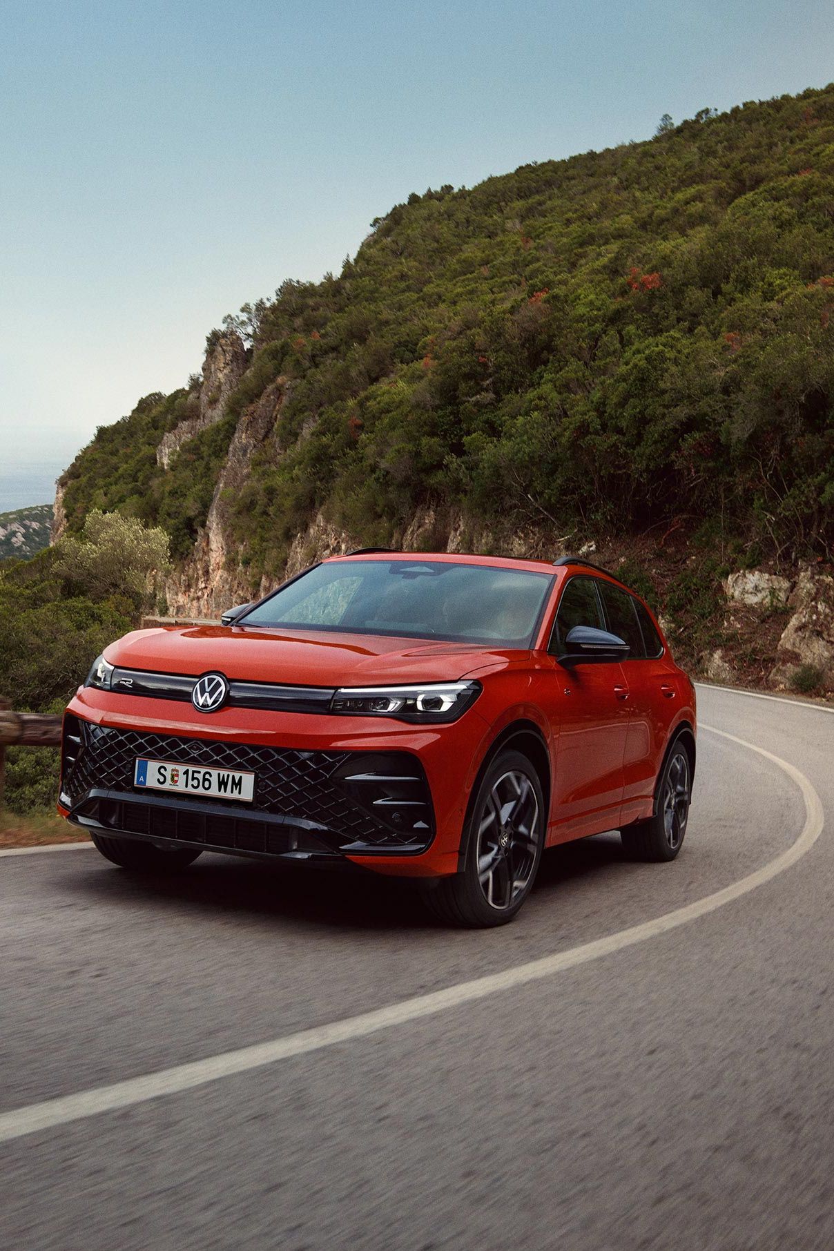 Rdeči VW Tiguan, ki vozi po ovinkasti cesti.