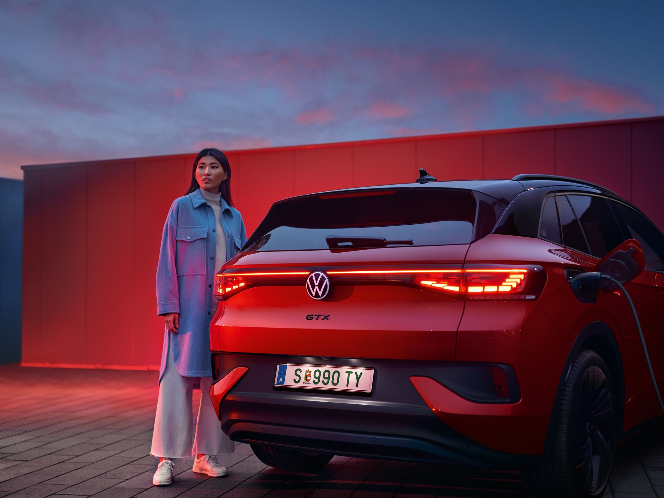 Rdeč VW ID.4 GTX je od zadaj prikazan med polnjenjem. Ob njem stoji ženska.
