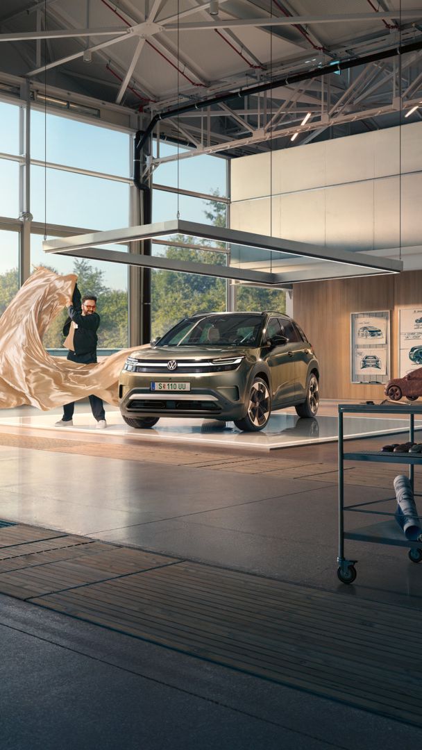 Moški odstranjuje veliko rjuho z zelenega VW ID. Crossa, ki stoji v minimalistično opremljenem oblikovalskem studiu.