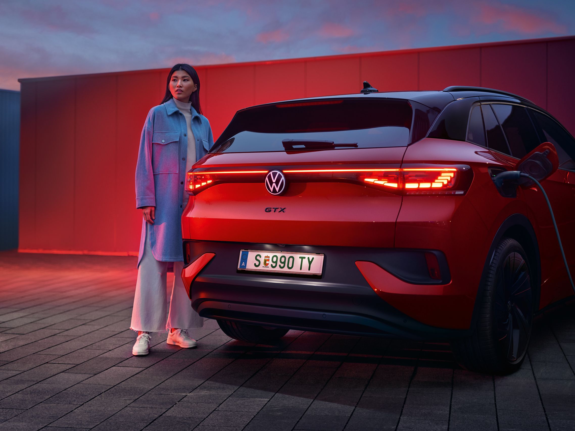 Rdeč VW ID.4 GTX je od zadaj prikazan med polnjenjem. Ob njem stoji ženska.