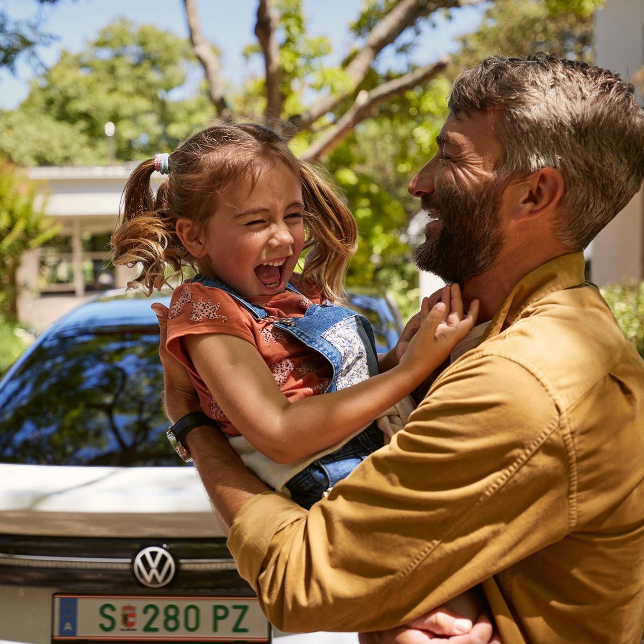 Ein Vater hält Kind im Arm, beide lachen, man sieht das Heck des VW ID.7