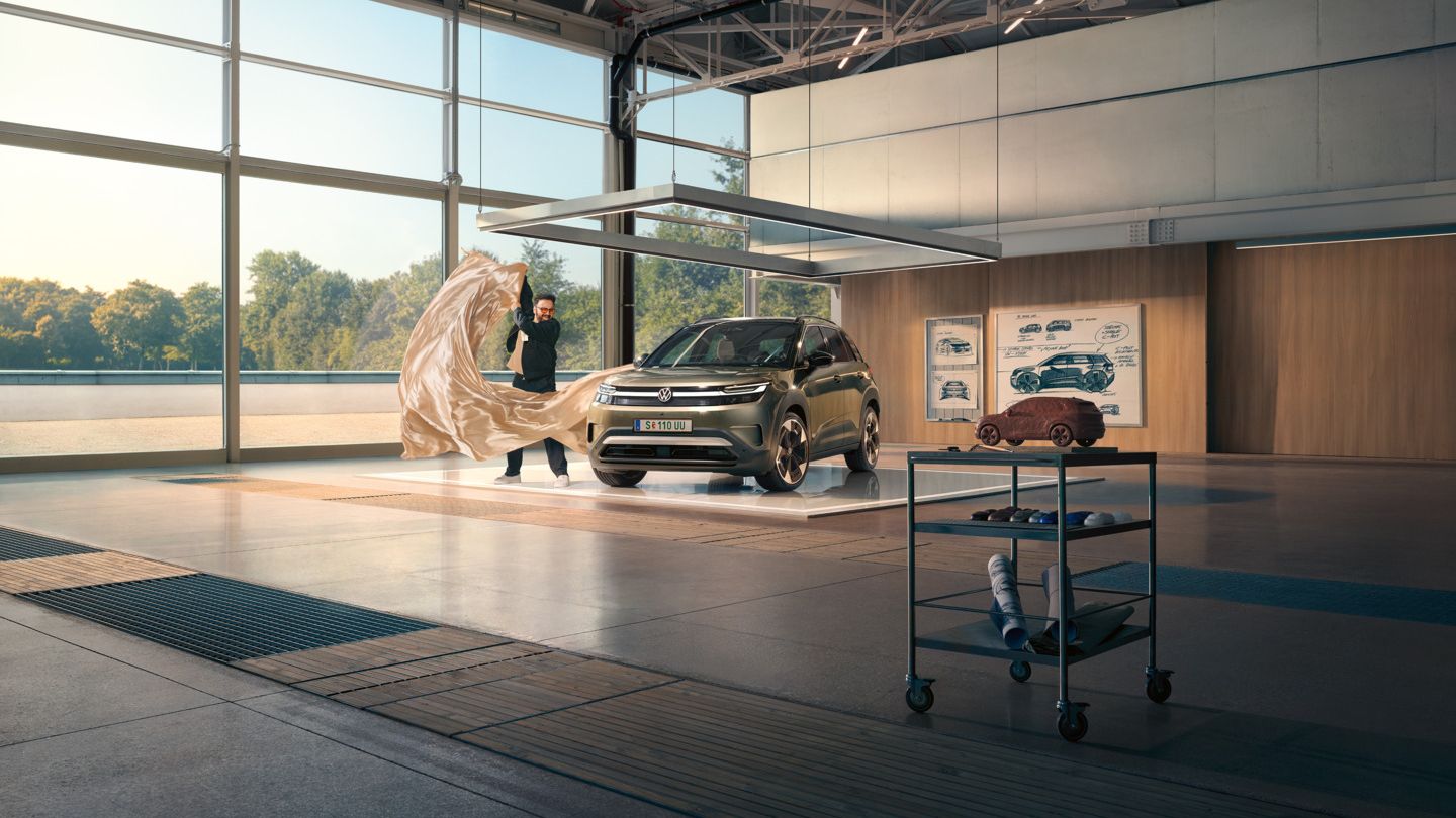 Moški odstranjuje veliko rjuho z zelenega VW ID. Crossa, ki stoji v minimalistično opremljenem oblikovalskem studiu.