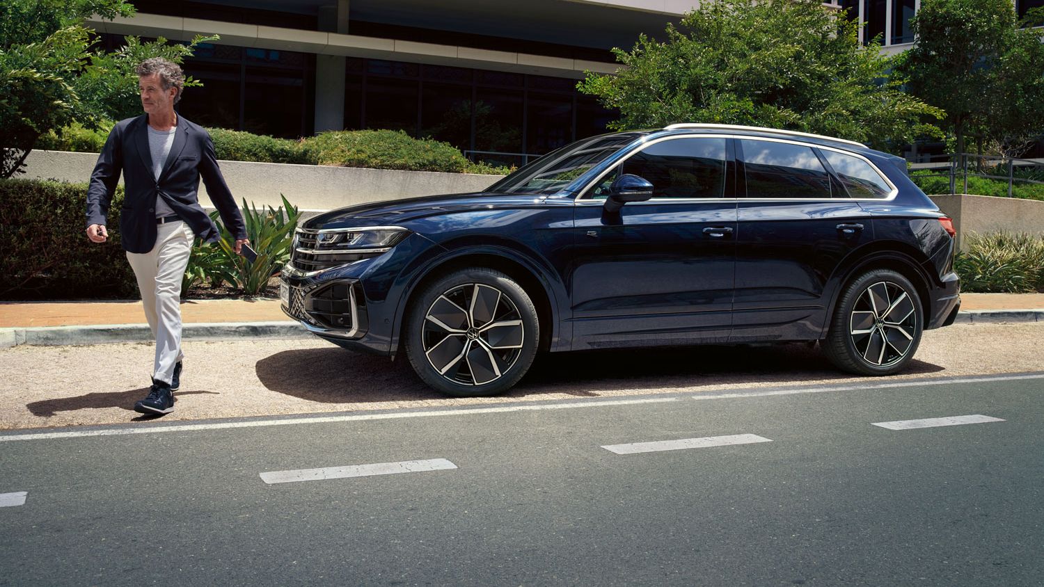 Moški prečka cesto, diagonalno za njim pa je ob robu ceste parkiran VW Touareg R-Line.