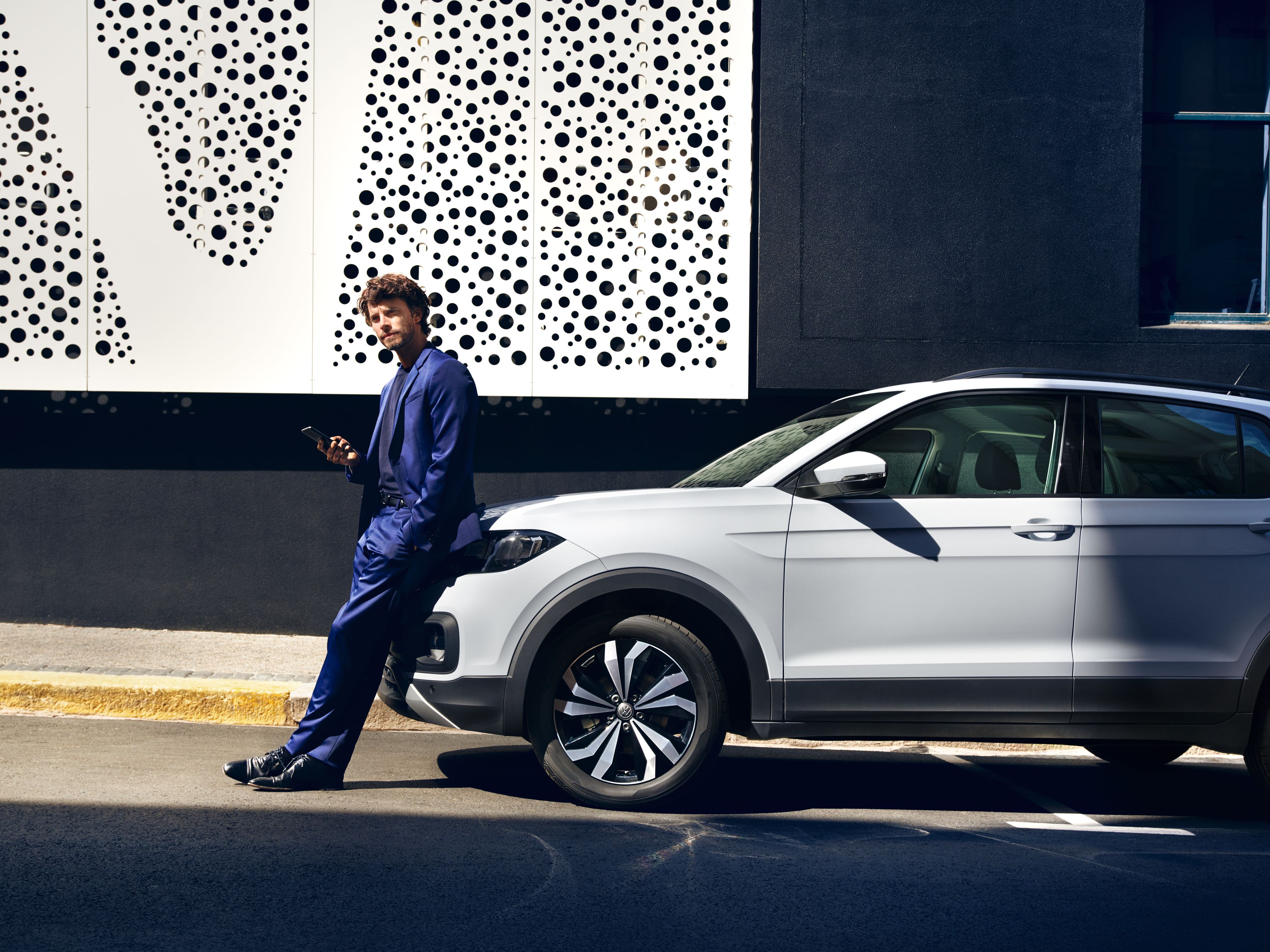 Mann lehnt an VW T-Cross mit Smartphone in der Hand und liest Newsletter