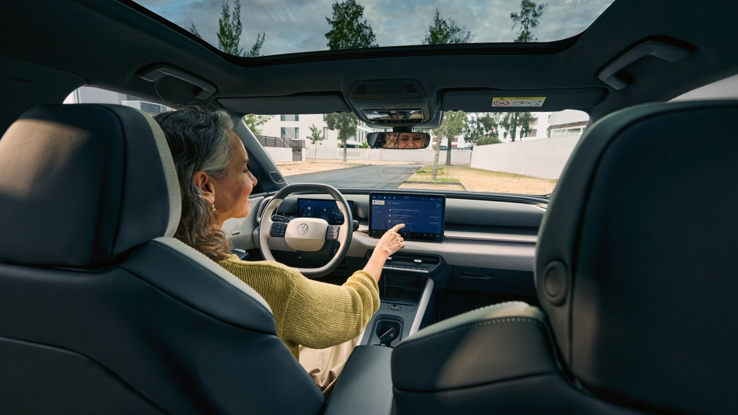 Ženska sedi na voznikovem sedežu VW ID. Crossa in upravlja infotainment sistem.