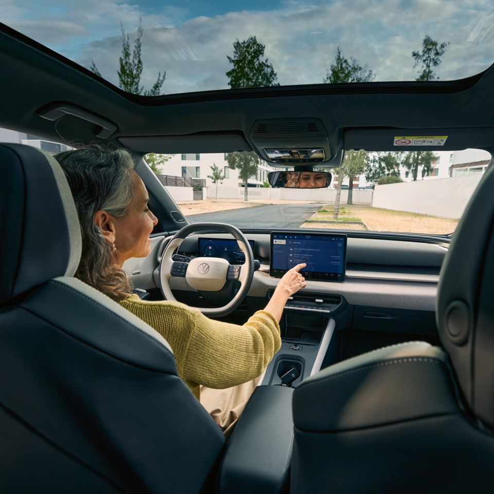 Ženska sedi na voznikovem sedežu VW ID. Crossa in upravlja infotainment sistem.