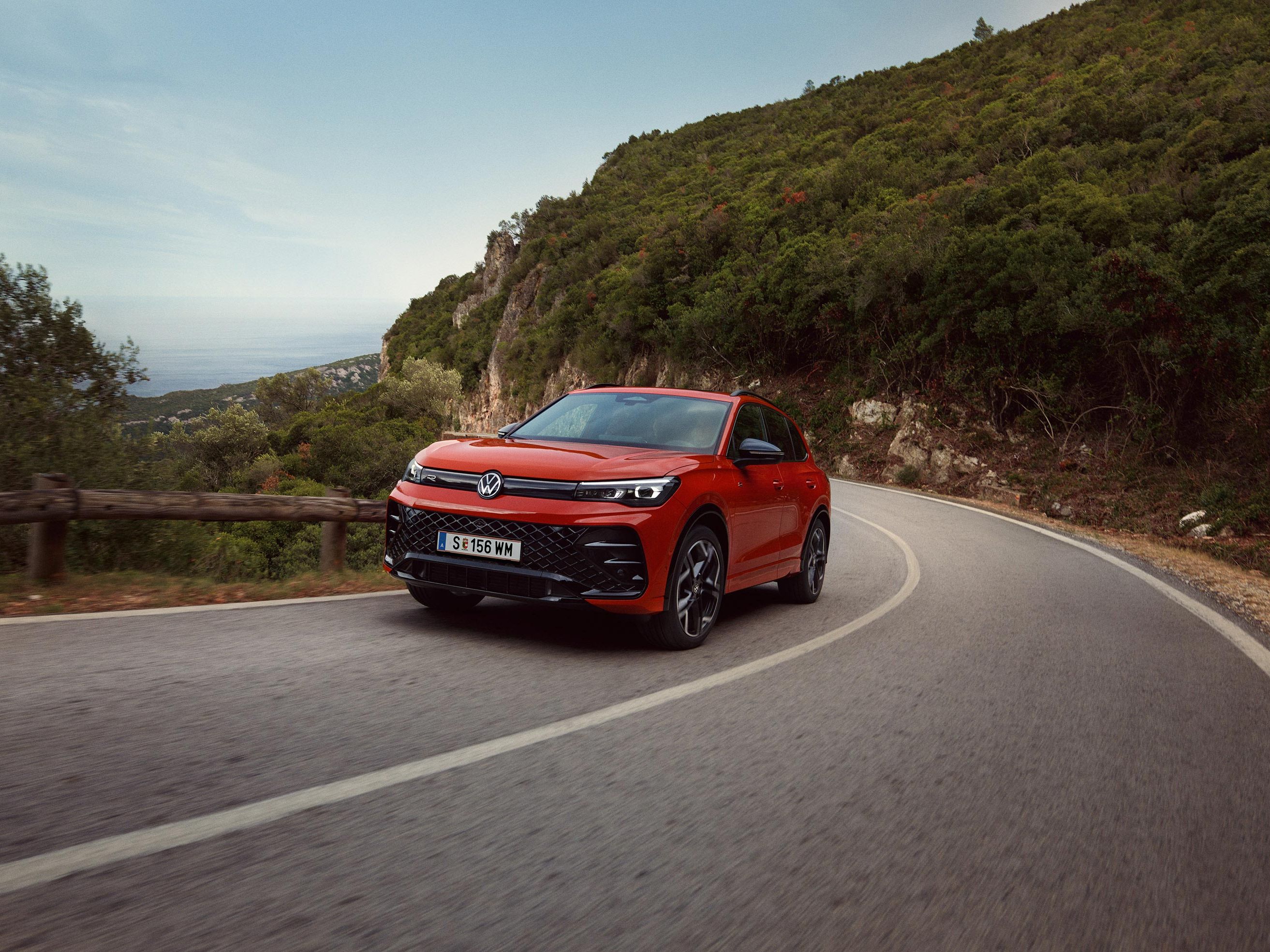 Rdeči VW Tiguan, ki vozi po ovinkasti cesti.