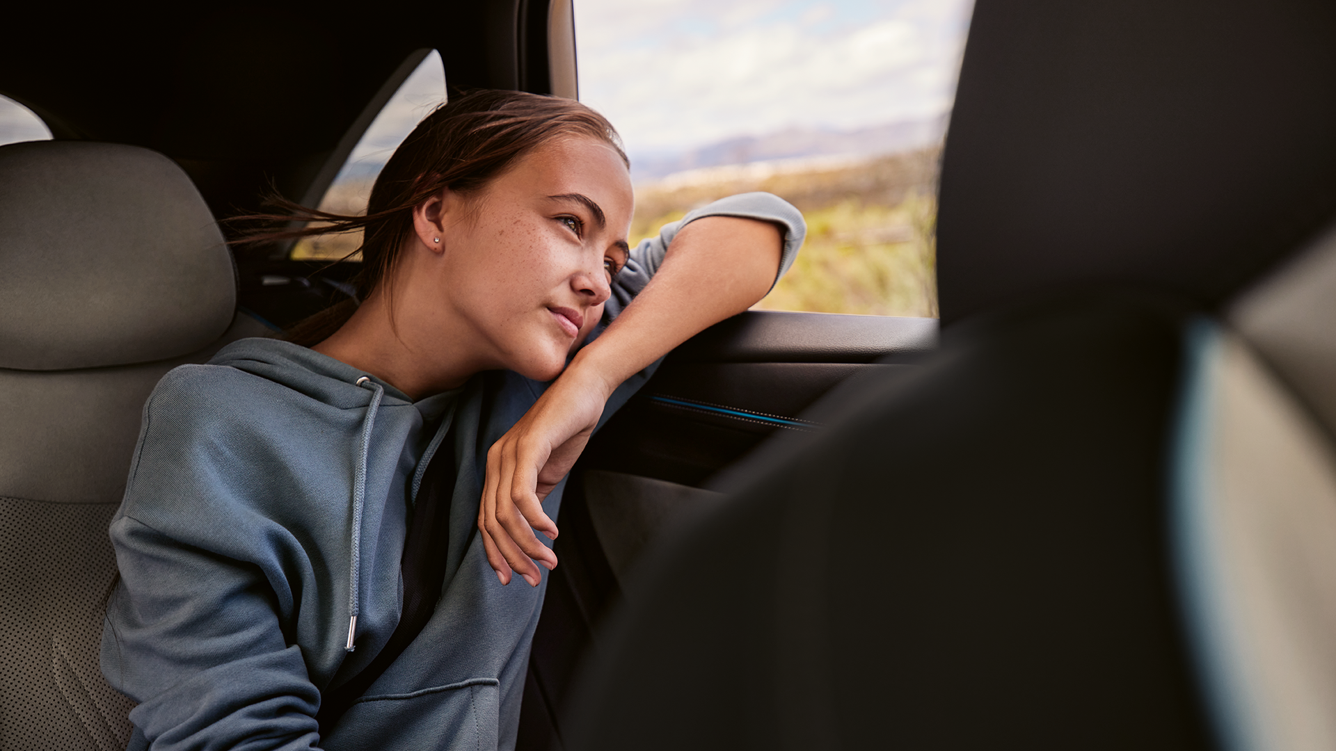 Mlada ženska na zadnjem sedežu VW ID.7 gleda skozi okno.