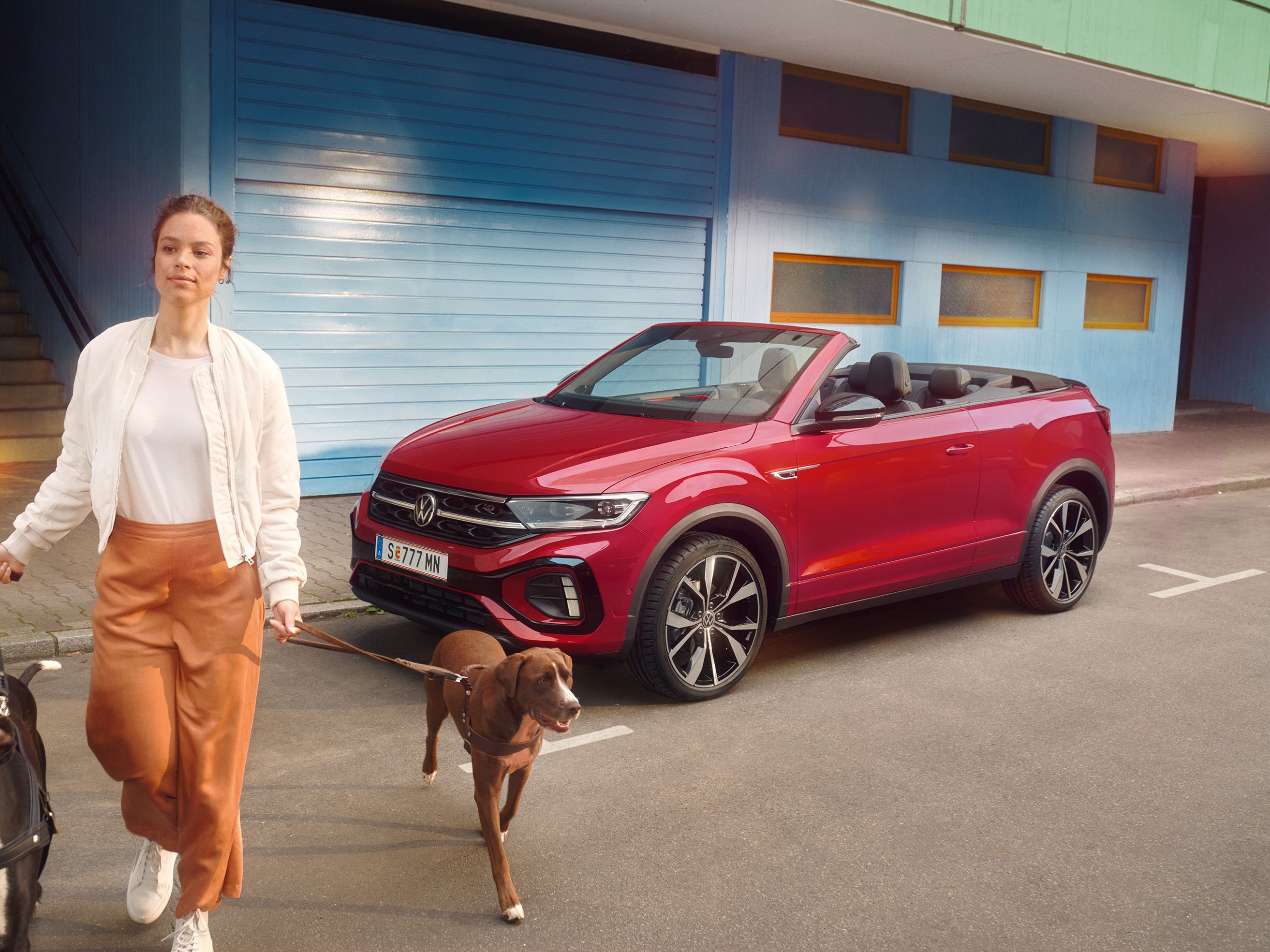 Frau geht mit zwei Hunden and der Leinen von einem roten VW T-Roc Cabrio weg