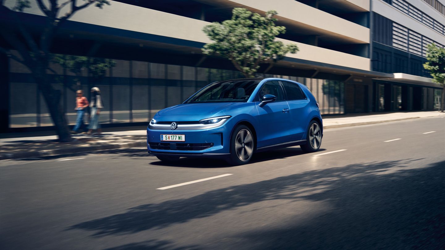 Moder VW ID. Polo Style vozi skozi mesto z zelenimi drevesi ob cesti.