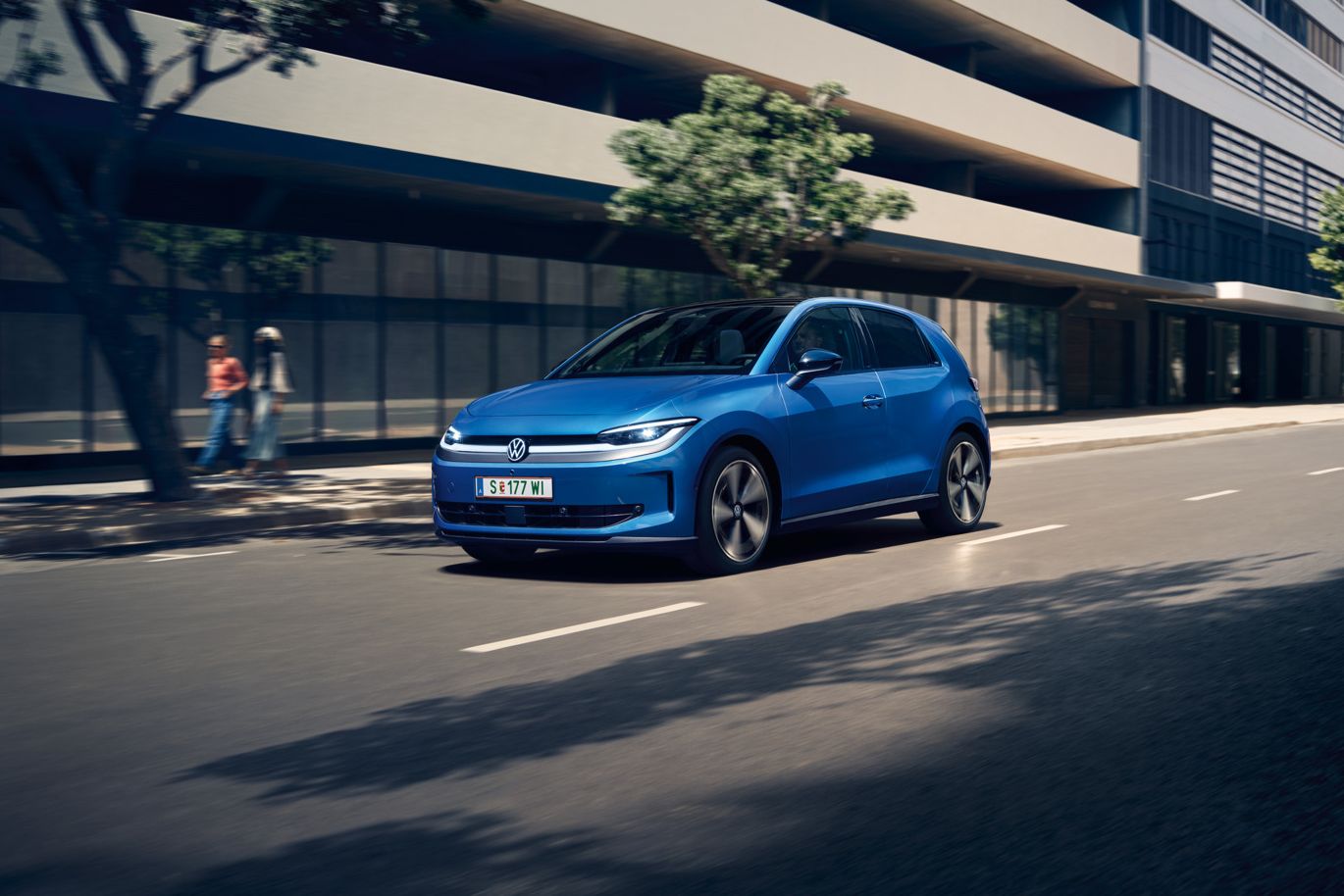 Moder VW ID. Polo Style vozi skozi mesto z zelenimi drevesi ob cesti.