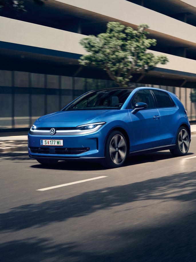 Moder VW ID. Polo Style vozi skozi mesto z zelenimi drevesi ob cesti.