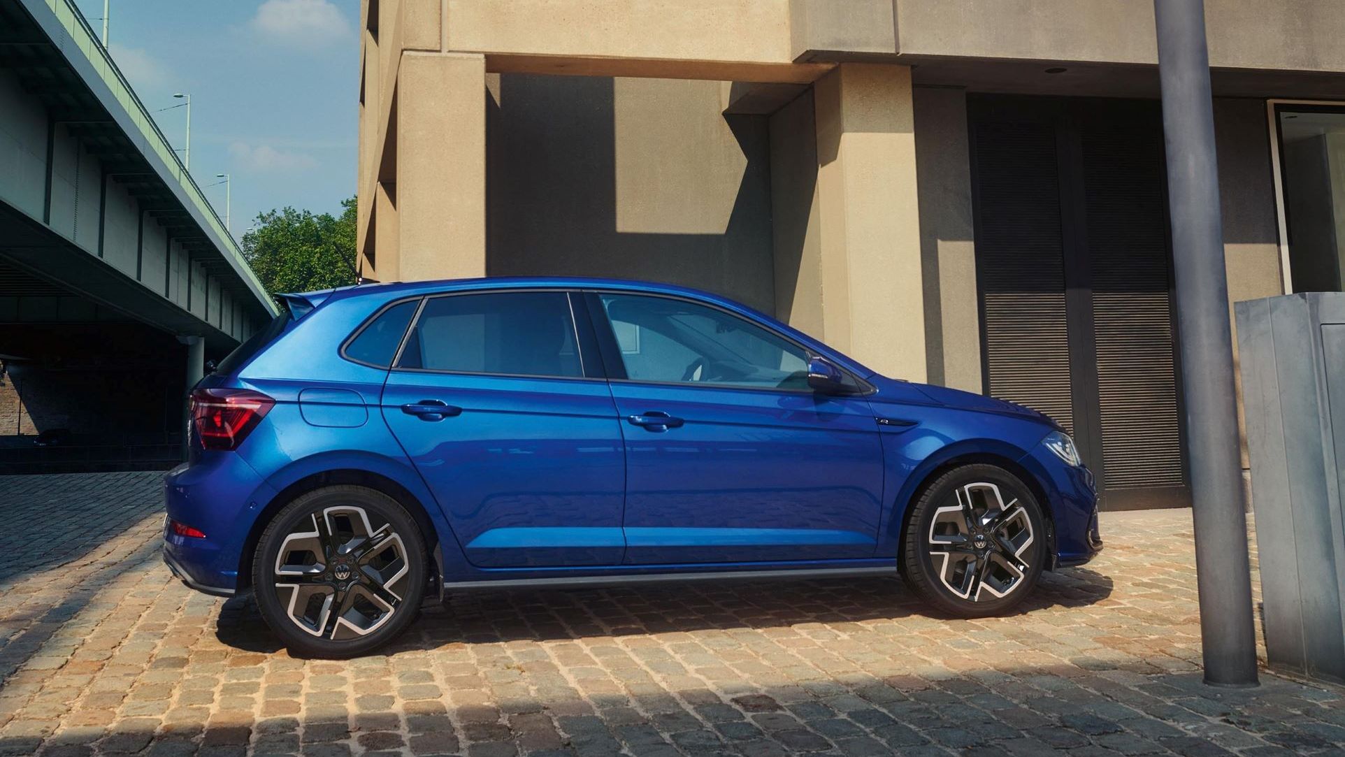 Prikaz sovoznikove strani modrega VW Pola, ki je parkiran pred stolpnico.