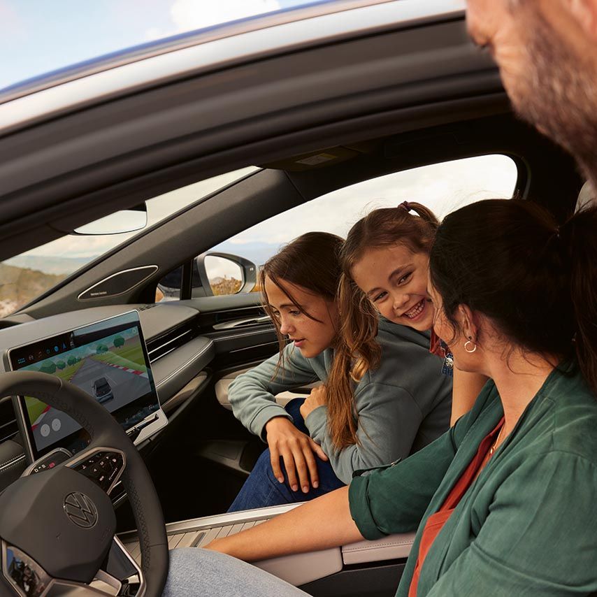 Dva otroka in ženska gledajo v infotainment sistem v stoječem ID.7, oče pa gleda skozi voznikova vrata.