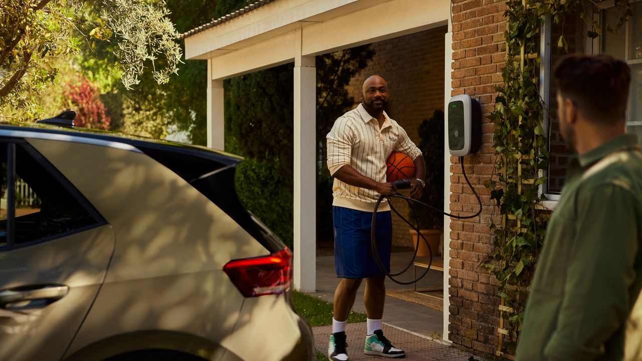 Moški se pogovarja s sosedom in drži polnilni kabel stenske polnilne postaje. V ospredju je Volkswagen ID.3 