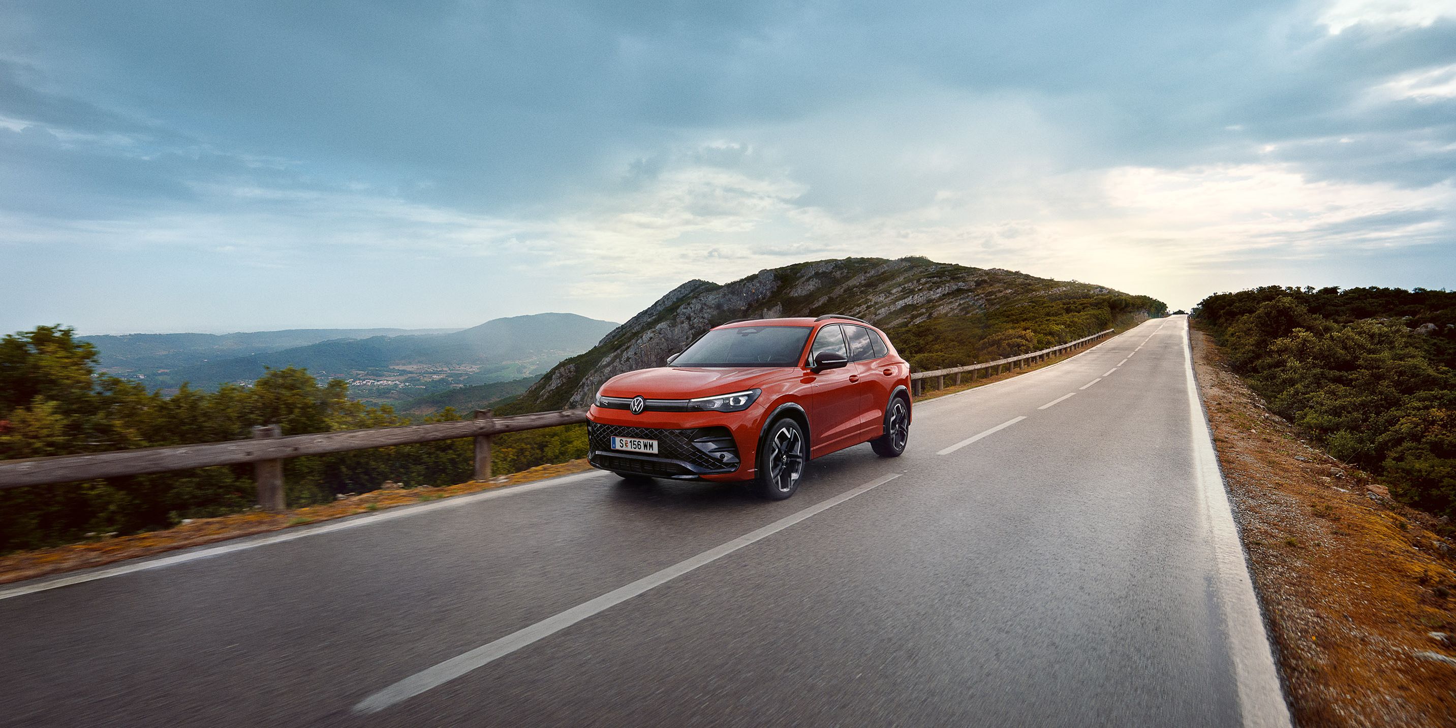 Rdeč VW Tiguan vozi po cesti.