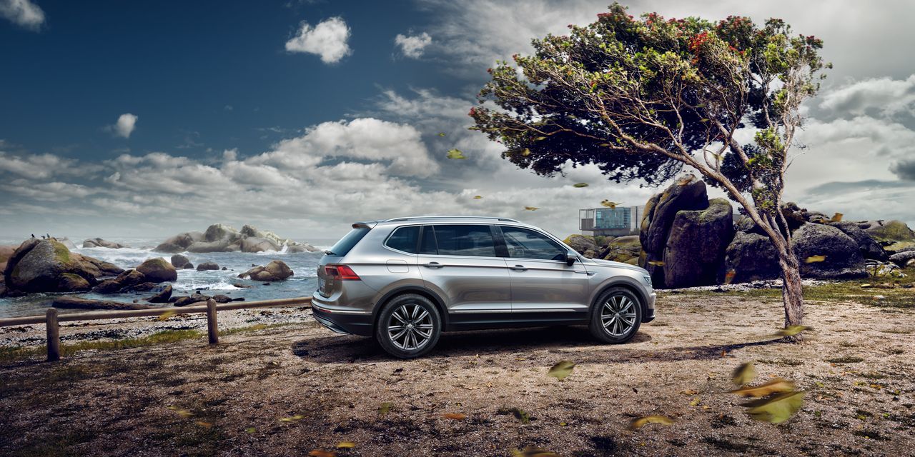 Srebrn VW Tiguan Allspace stoji ob obali, pod osamljenim drevesom. V ozadju so skalnati bregovi in morje pod oblačnim nebom. Listje na tleh nakazuje vetrovno vreme.