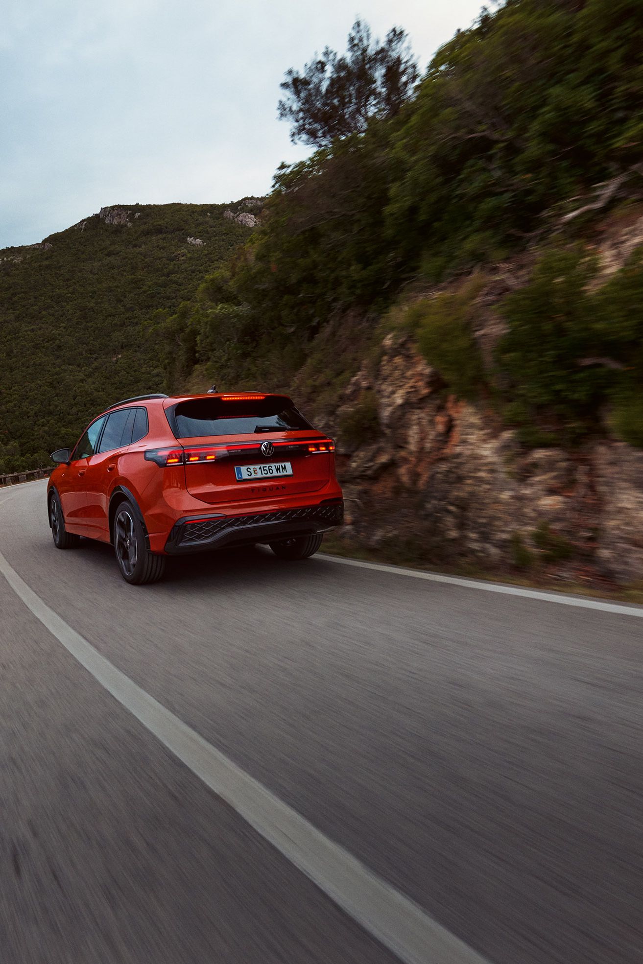 Pogled od zadaj na rdeč VW Tiguan, ki vozi po gorski pokrajini.