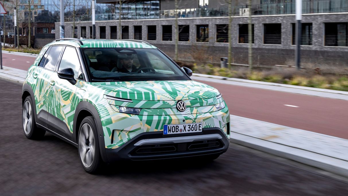 Električni Volkswagen SUV se pelje mimo sodobnih stavb na mestni ulici. Vozilo ima vpadljiv dizajn z zelenimi in rumenimi vzorci. 