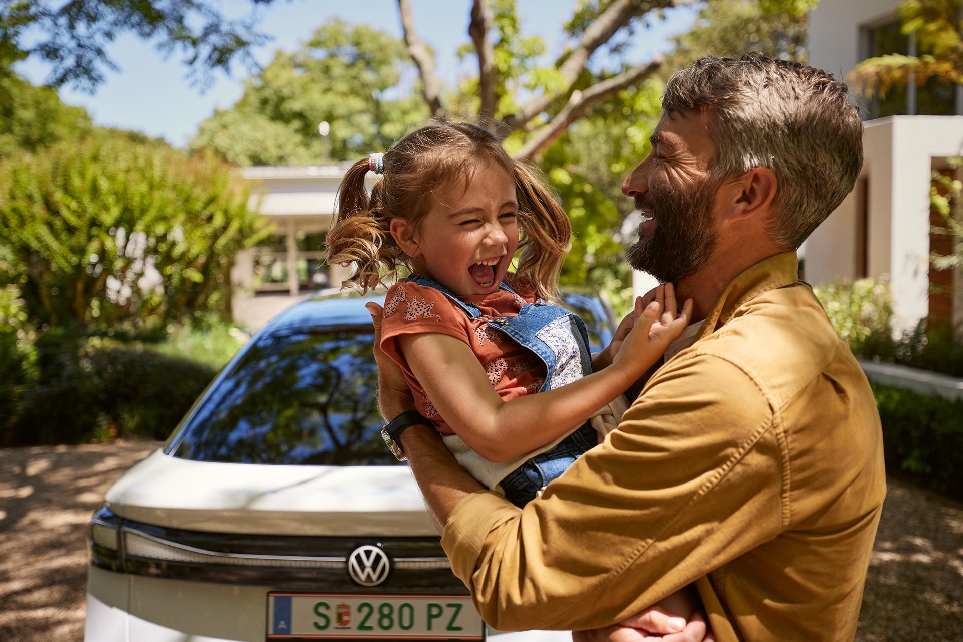 Ein Vater hält Kind im Arm, beide lachen, man sieht das Heck des VW ID.7