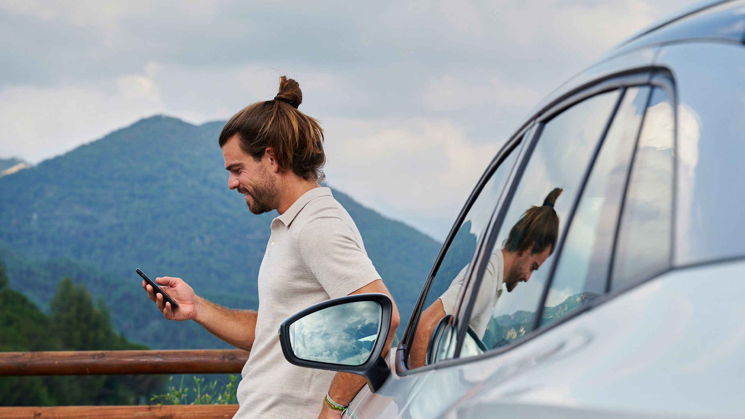 Ein Mann lehnt an einem Volkswagen ID. und blickt auf sein Smartphone.