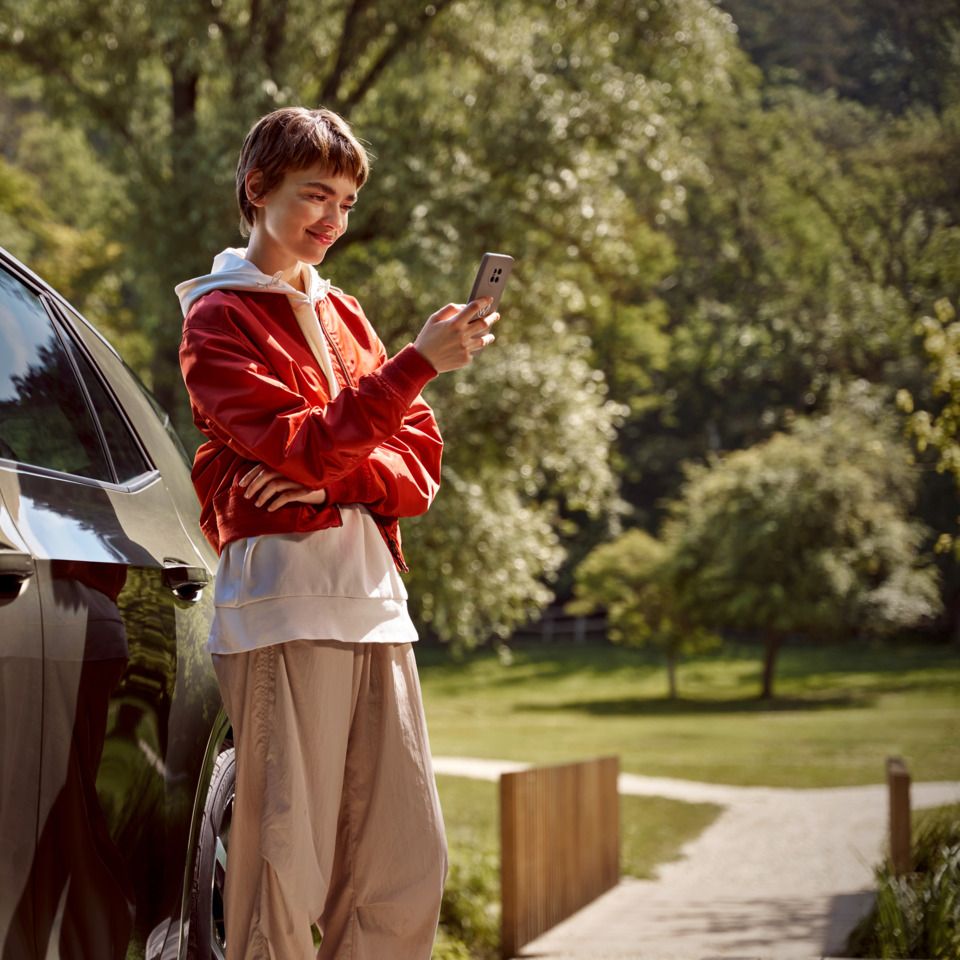 Ženska s pametnim telefonom stoji desno poleg modela Volkswagen ID.3