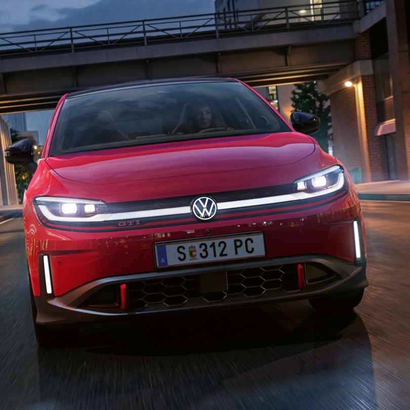 Oseba zvečer vozi rdeč VW ID. Polo GTI skozi sodobno osvetljeno poslovno četrt.