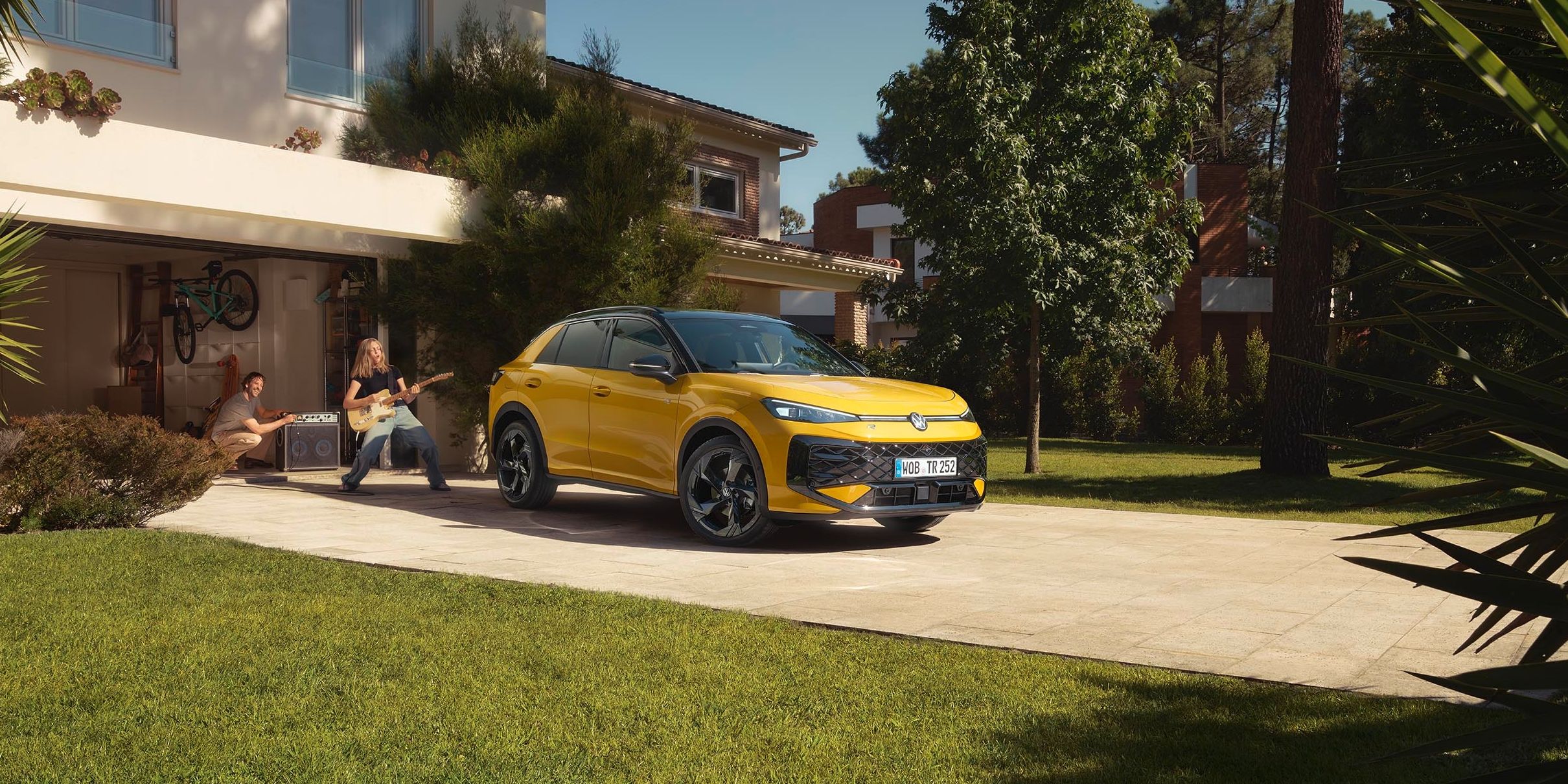 Rumeni VW T-Roc je parkiran pred moderno hišo z lepo urejenim dvoriščem in zelenico. 