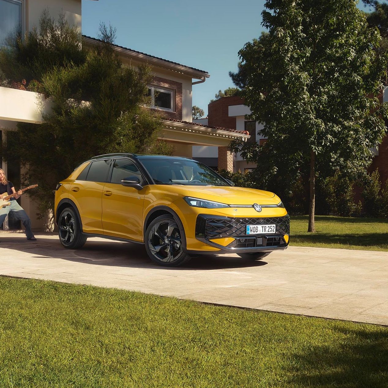 Rumeni VW T-Roc je parkiran pred moderno hišo z lepo urejenim dvoriščem in zelenico. 