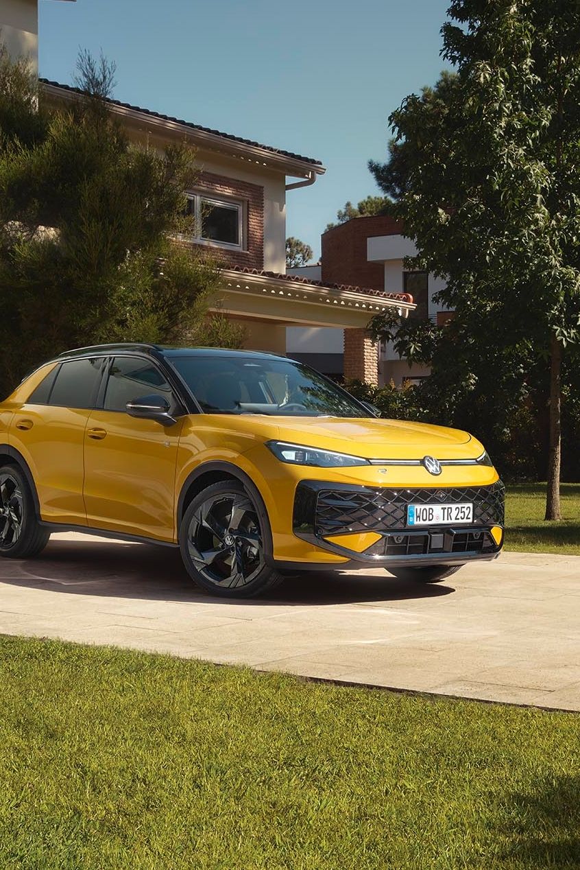 Rumeni VW T-Roc je parkiran pred moderno hišo z lepo urejenim dvoriščem in zelenico. 