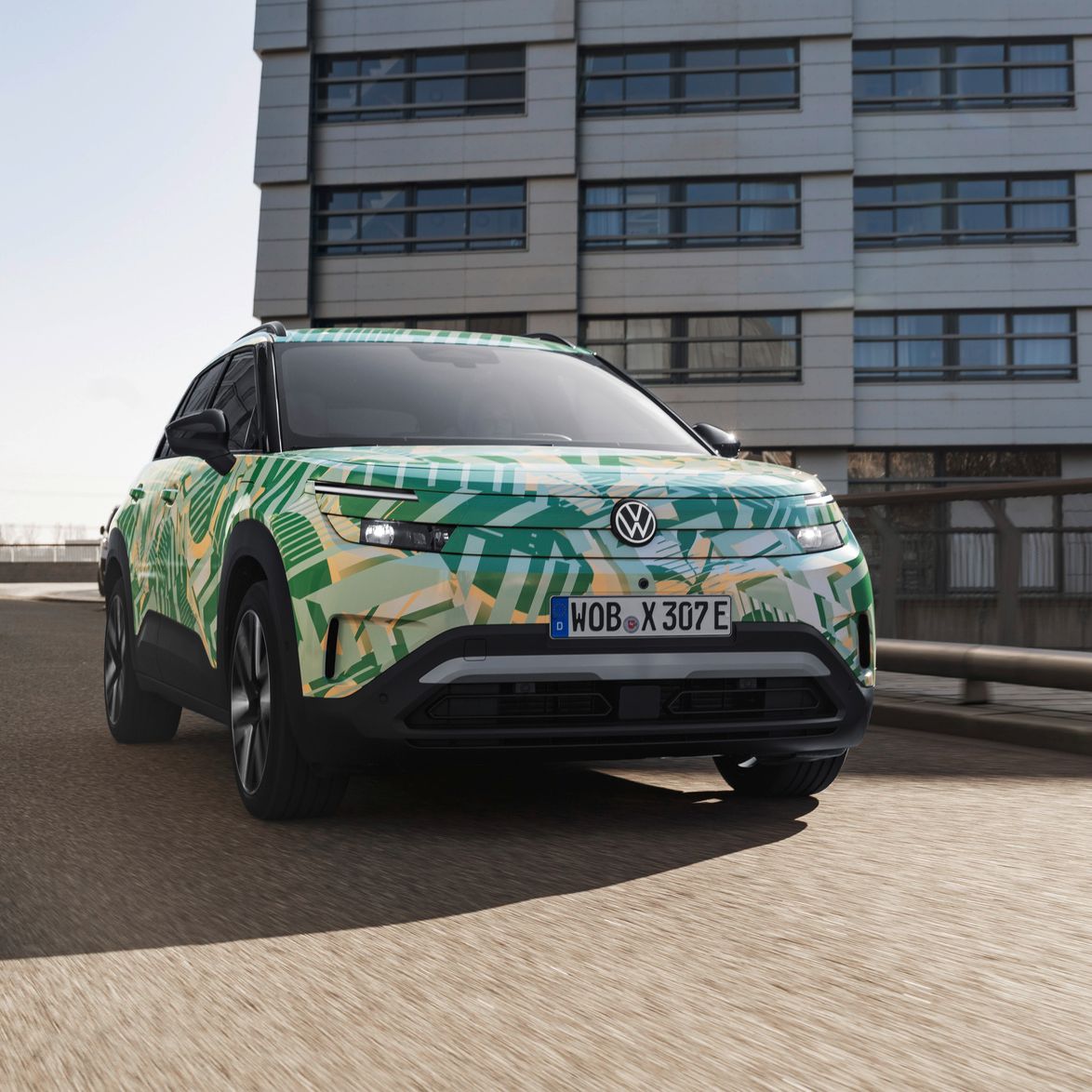 VW ID. Cross z maskirno folijo na mestni parkirni ploščadi pred sodobno stolpnico.