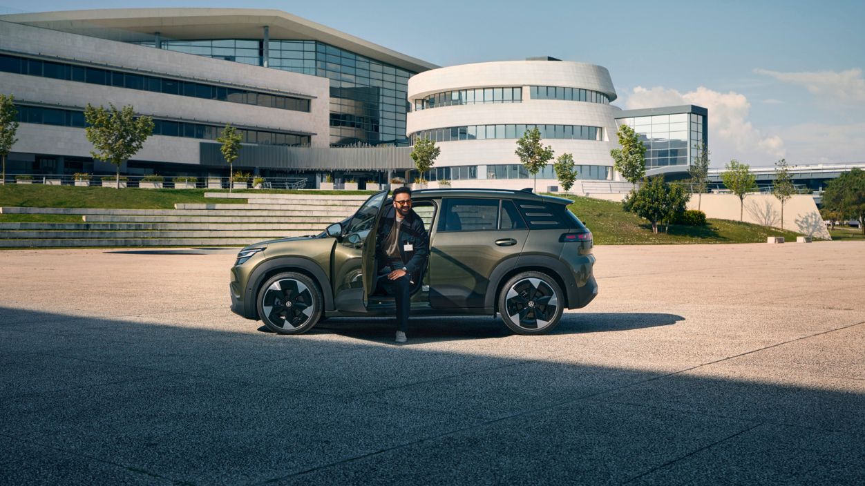 Moški izstopa skozi voznikova vrata VW ID. Crossa, ki stoji pred sodobno večnadstropno poslovno stavbo.